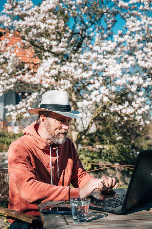 Arwed Grön (GROENIE) am Laptop im Garten des HALE ALOHA in Schleswig-Holstein. Im Hintergrund die blühende Magnolie.